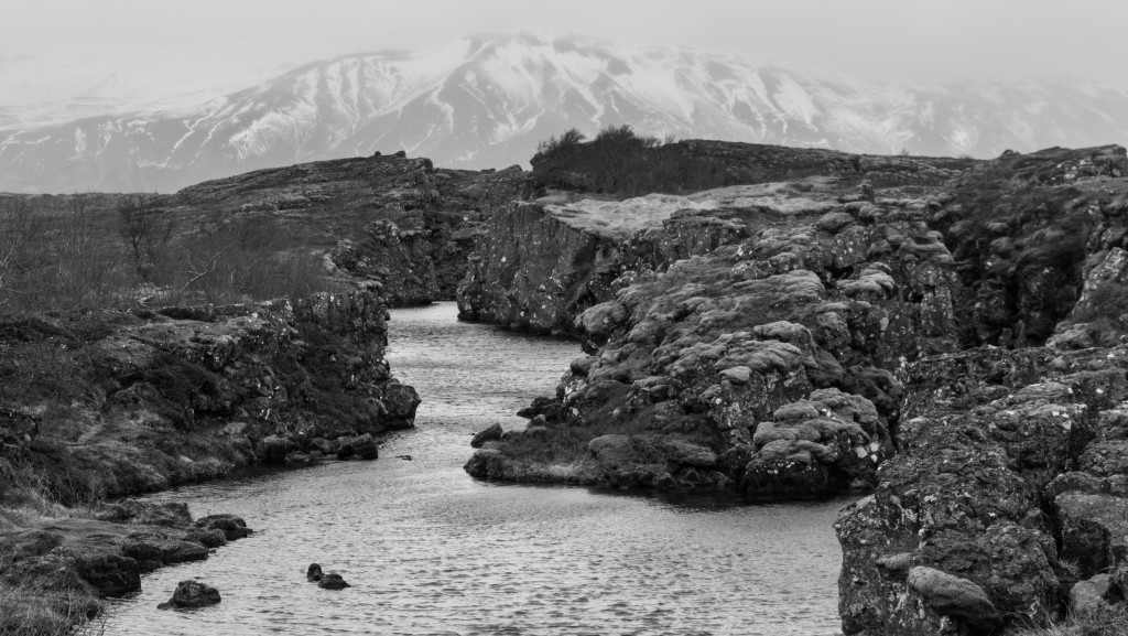 Geology in Iceland shows as a stream flowing through a ridge with mountains as background setting